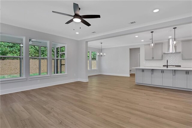 unfurnished living room featuring ceiling fan with notable chandelier and light hardwood / wood-style floors