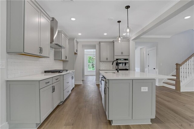 kitchen with gray cabinetry, a center island with sink, light hardwood / wood-style flooring, and wall chimney range hood