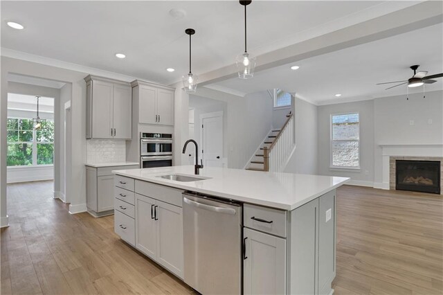 kitchen with ceiling fan, an island with sink, sink, stainless steel appliances, and light wood-type flooring