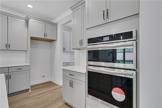 kitchen featuring gray cabinets, light wood-type flooring, backsplash, and double oven