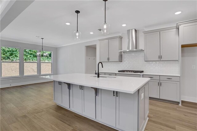 kitchen featuring light hardwood / wood-style floors, wall chimney exhaust hood, gray cabinets, black gas cooktop, and a kitchen island with sink