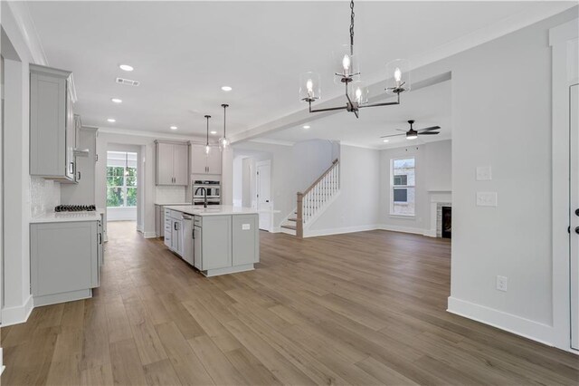 kitchen with ceiling fan with notable chandelier, pendant lighting, stainless steel oven, light wood-type flooring, and a center island with sink