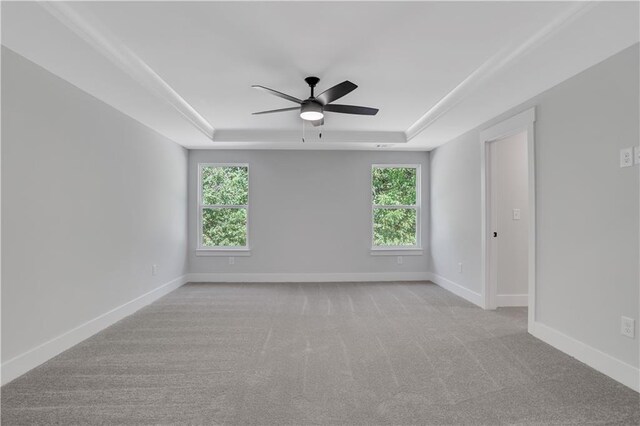 empty room with a tray ceiling, ceiling fan, light colored carpet, and plenty of natural light