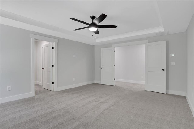 unfurnished bedroom with light carpet, a tray ceiling, and ceiling fan