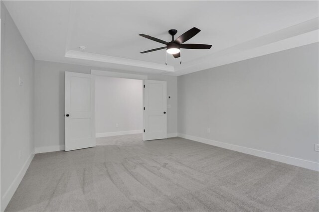 empty room with ceiling fan, a tray ceiling, and light carpet