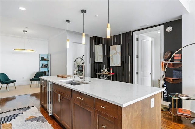 kitchen with sink, hanging light fixtures, dark wood-type flooring, wine cooler, and a kitchen island with sink