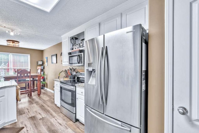 835 Custom Ln, Winder, GA 30680 - kitchen with stainless steel appliances, a textured ceiling, white cabinetry, light wood-type flooring, and light stone countertops