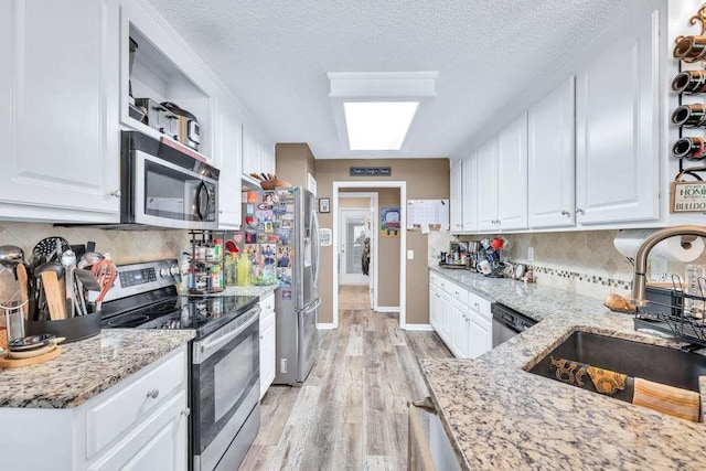 835 Custom Ln, Winder, GA 30680 - kitchen with appliances with stainless steel finishes, a sink, white cabinets, light wood-type flooring, and decorative backsplash
