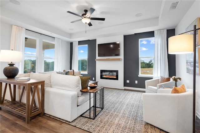 living room with ceiling fan, plenty of natural light, hardwood / wood-style floors, and a raised ceiling