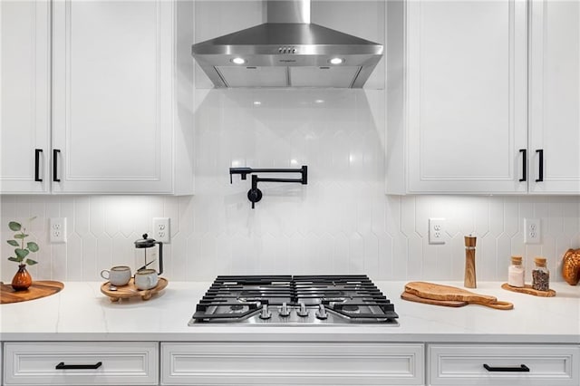 kitchen featuring white cabinets, wall chimney exhaust hood, backsplash, stainless steel gas cooktop, and light stone counters