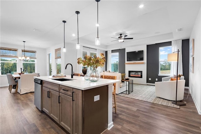 kitchen with dishwasher, decorative light fixtures, sink, dark wood-type flooring, and a kitchen island with sink