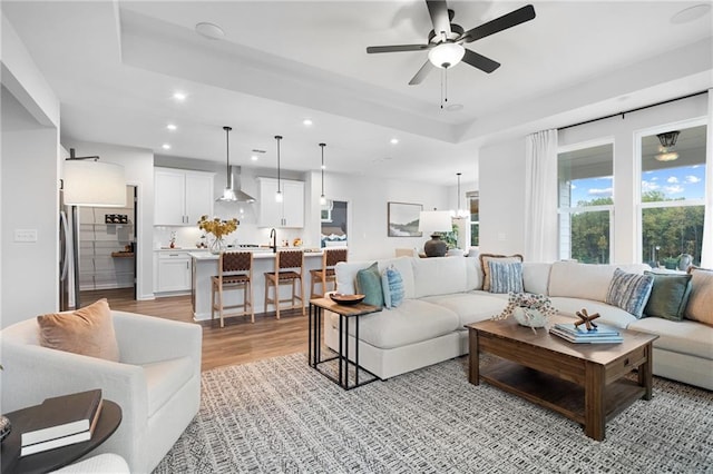 living room featuring ceiling fan, light hardwood / wood-style floors, sink, and a tray ceiling