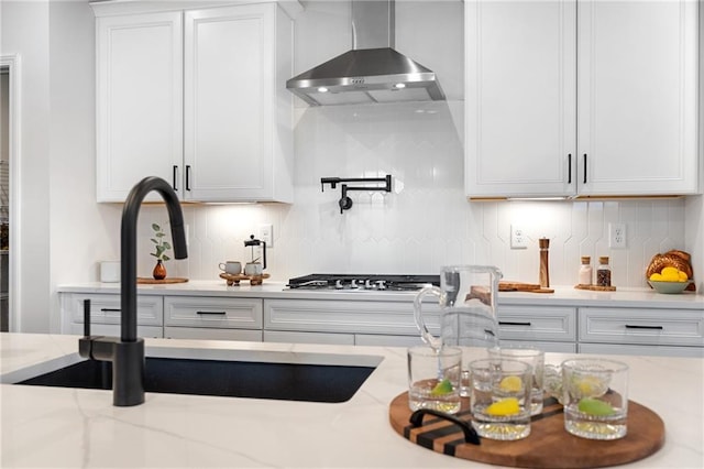 kitchen with white cabinets, wall chimney exhaust hood, backsplash, stainless steel gas cooktop, and light stone counters