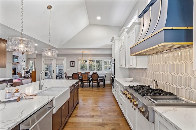 kitchen featuring vaulted ceiling, appliances with stainless steel finishes, white cabinetry, hanging light fixtures, and custom range hood