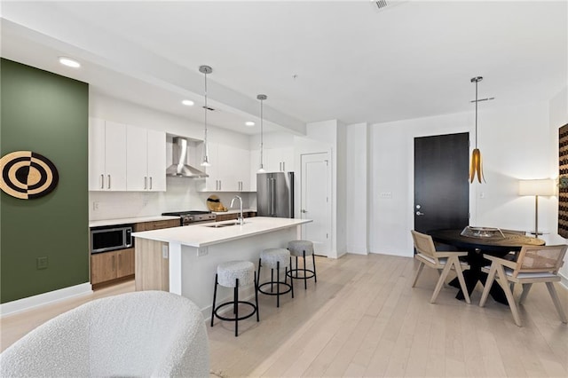 kitchen with sink, appliances with stainless steel finishes, white cabinetry, decorative light fixtures, and wall chimney exhaust hood