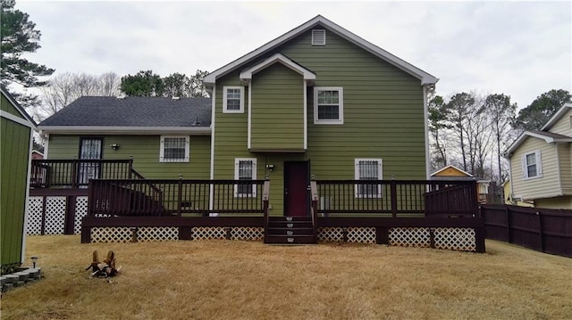 back of property featuring fence, a wooden deck, and a lawn