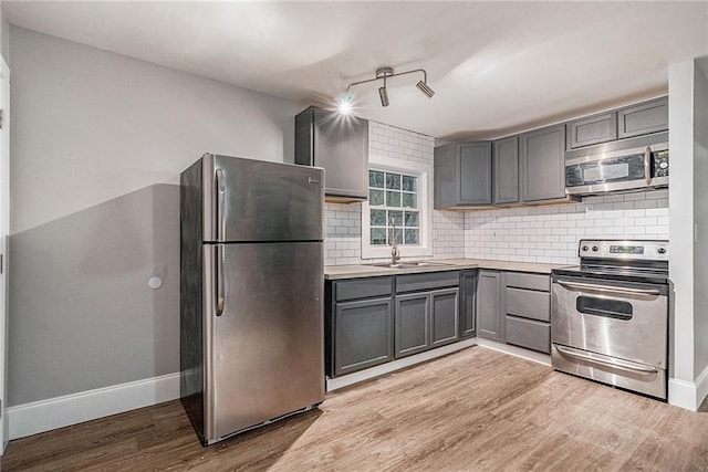 kitchen with tasteful backsplash, light hardwood / wood-style floors, stainless steel appliances, sink, and gray cabinets