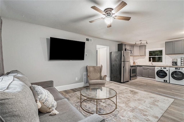 living room featuring washing machine and dryer, ceiling fan, sink, and light hardwood / wood-style floors