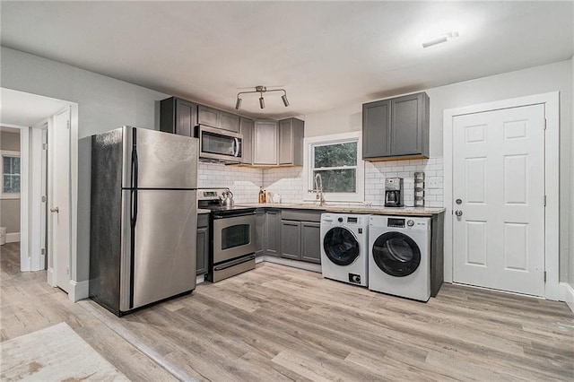 kitchen featuring washing machine and clothes dryer, gray cabinets, stainless steel appliances, and light hardwood / wood-style floors