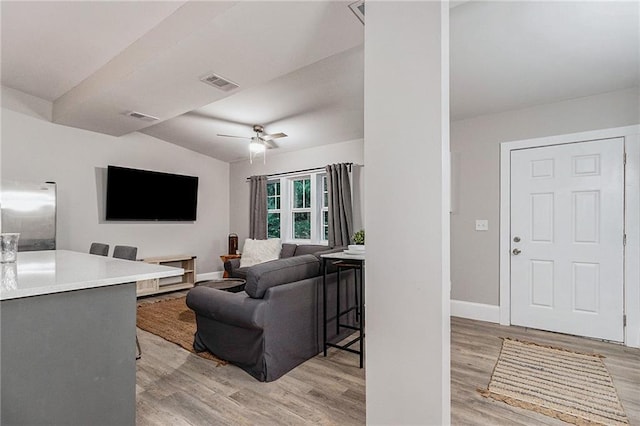 living room with ceiling fan, vaulted ceiling, and light wood-type flooring