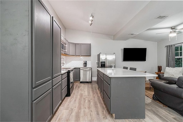 kitchen with decorative backsplash, appliances with stainless steel finishes, light hardwood / wood-style floors, gray cabinets, and an island with sink