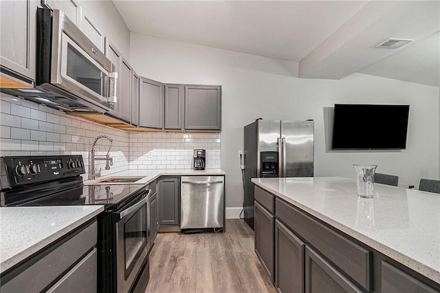 kitchen with decorative backsplash, wood-type flooring, sink, and appliances with stainless steel finishes