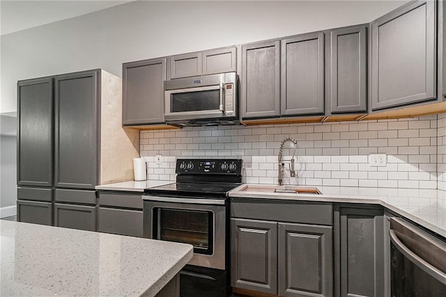 kitchen with stainless steel appliances, gray cabinets, tasteful backsplash, and sink