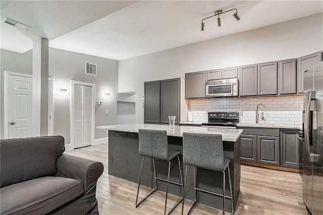 kitchen featuring sink, stainless steel appliances, light hardwood / wood-style floors, and an island with sink