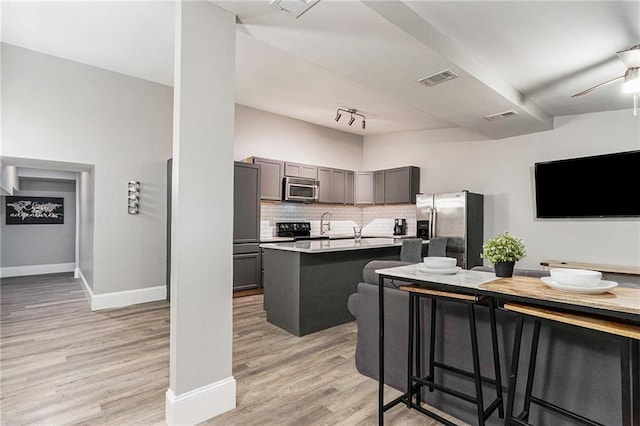 kitchen with a kitchen breakfast bar, light hardwood / wood-style floors, appliances with stainless steel finishes, tasteful backsplash, and a kitchen island