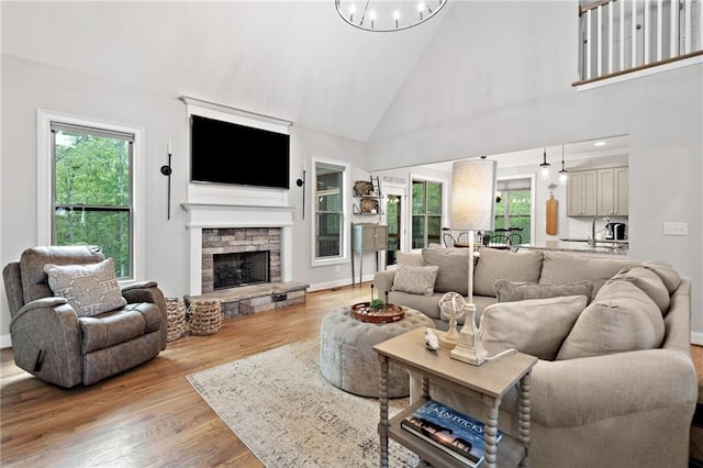 living area with wood finished floors, a stone fireplace, baseboards, high vaulted ceiling, and a chandelier