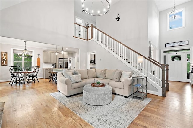 living room with an inviting chandelier, a high ceiling, stairs, and light wood-style flooring