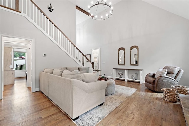 living area featuring a notable chandelier, high vaulted ceiling, stairs, baseboards, and wood finished floors