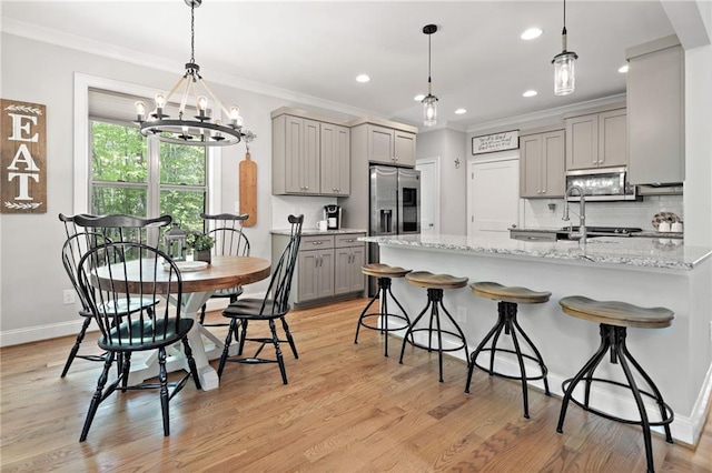 kitchen with crown molding, a breakfast bar, appliances with stainless steel finishes, a notable chandelier, and gray cabinetry