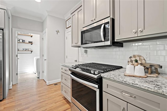kitchen featuring ornamental molding, light stone countertops, light wood-style floors, tasteful backsplash, and appliances with stainless steel finishes