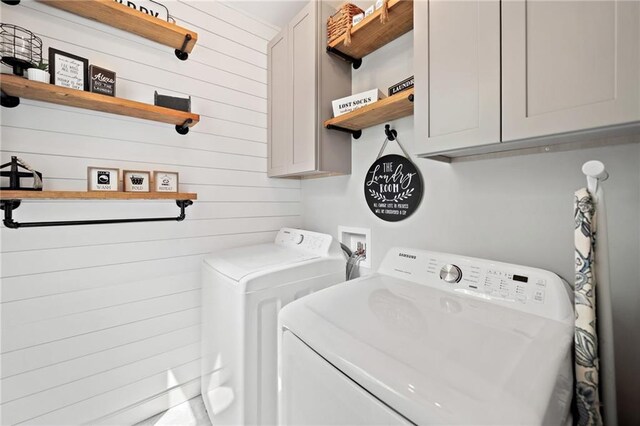 washroom featuring cabinet space, wood walls, and washing machine and dryer