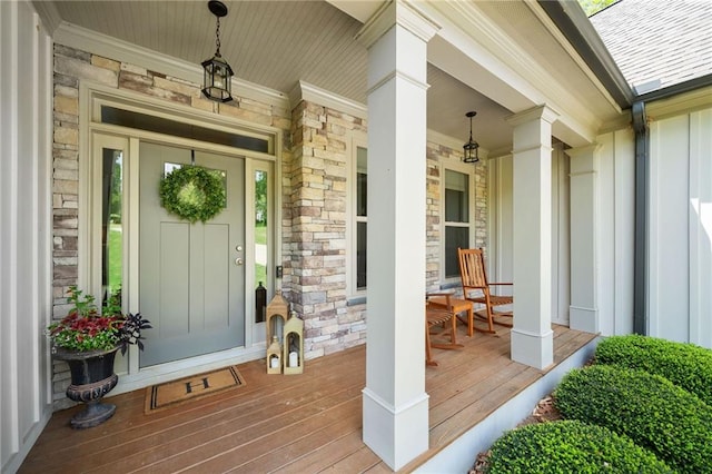 doorway to property with covered porch, board and batten siding, a shingled roof, and stone siding