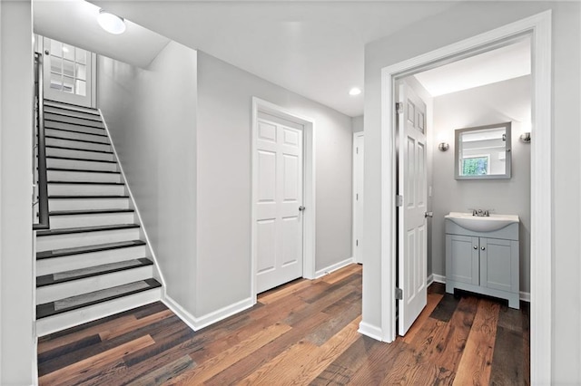 hallway featuring a sink, dark wood finished floors, recessed lighting, baseboards, and stairway