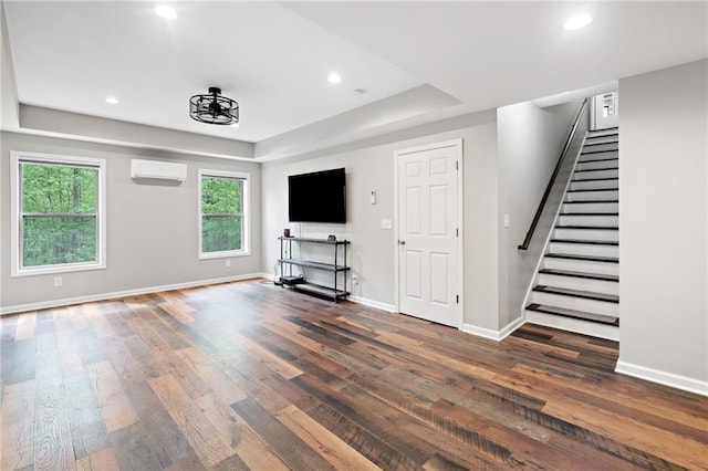 unfurnished living room featuring wood finished floors, baseboards, stairway, an AC wall unit, and a tray ceiling