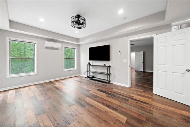 unfurnished living room featuring a raised ceiling, plenty of natural light, a wall mounted AC, and wood finished floors