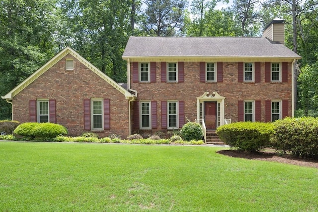 colonial home with a chimney, a front lawn, and brick siding