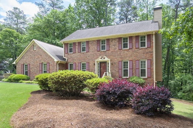 colonial home featuring a chimney, brick siding, a front lawn, and roof with shingles