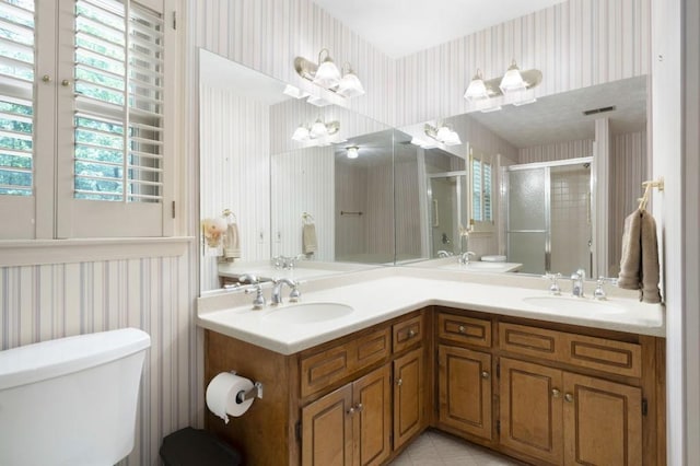 bathroom featuring wallpapered walls, toilet, a shower stall, double vanity, and tile patterned floors