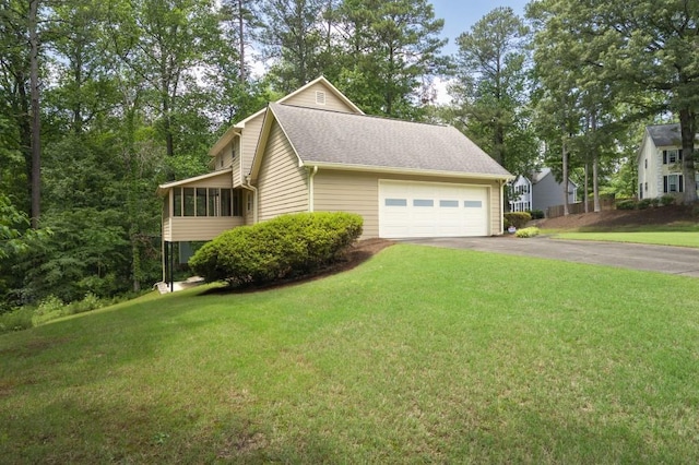 view of side of home featuring asphalt driveway, an attached garage, a yard, a sunroom, and roof with shingles