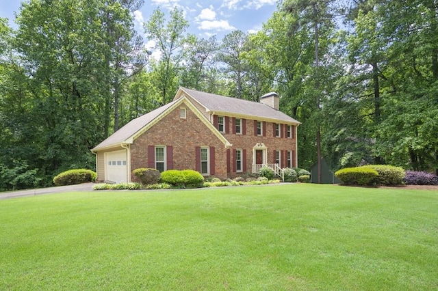 colonial home featuring a chimney, a front lawn, asphalt driveway, an attached garage, and brick siding
