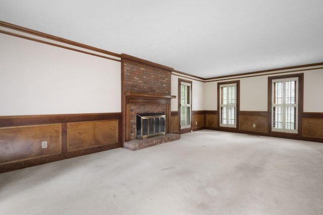 unfurnished living room with wainscoting, light carpet, crown molding, and a fireplace