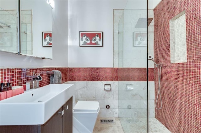 bathroom with a tile shower, backsplash, toilet, vanity, and tile walls