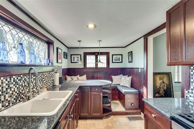 kitchen with sink, dark stone counters, decorative light fixtures, and ornamental molding