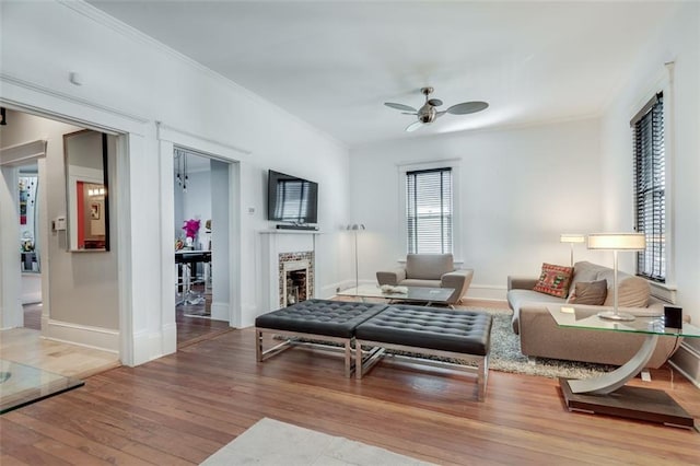 living room featuring ceiling fan, wood-type flooring, crown molding, and a brick fireplace