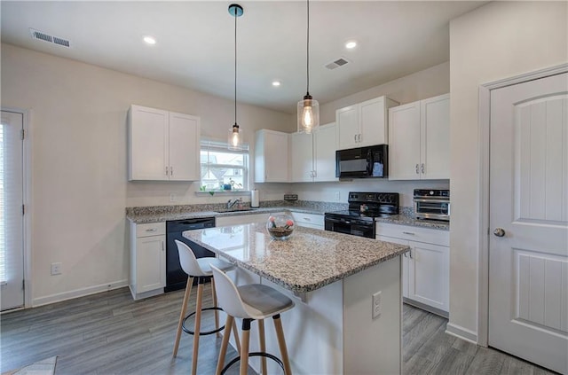 kitchen with white cabinetry, a center island, a breakfast bar, and black appliances