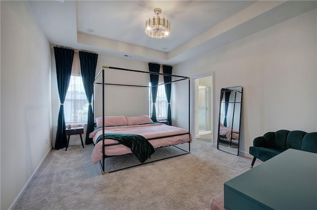 bedroom with a notable chandelier, a tray ceiling, light colored carpet, and ensuite bathroom